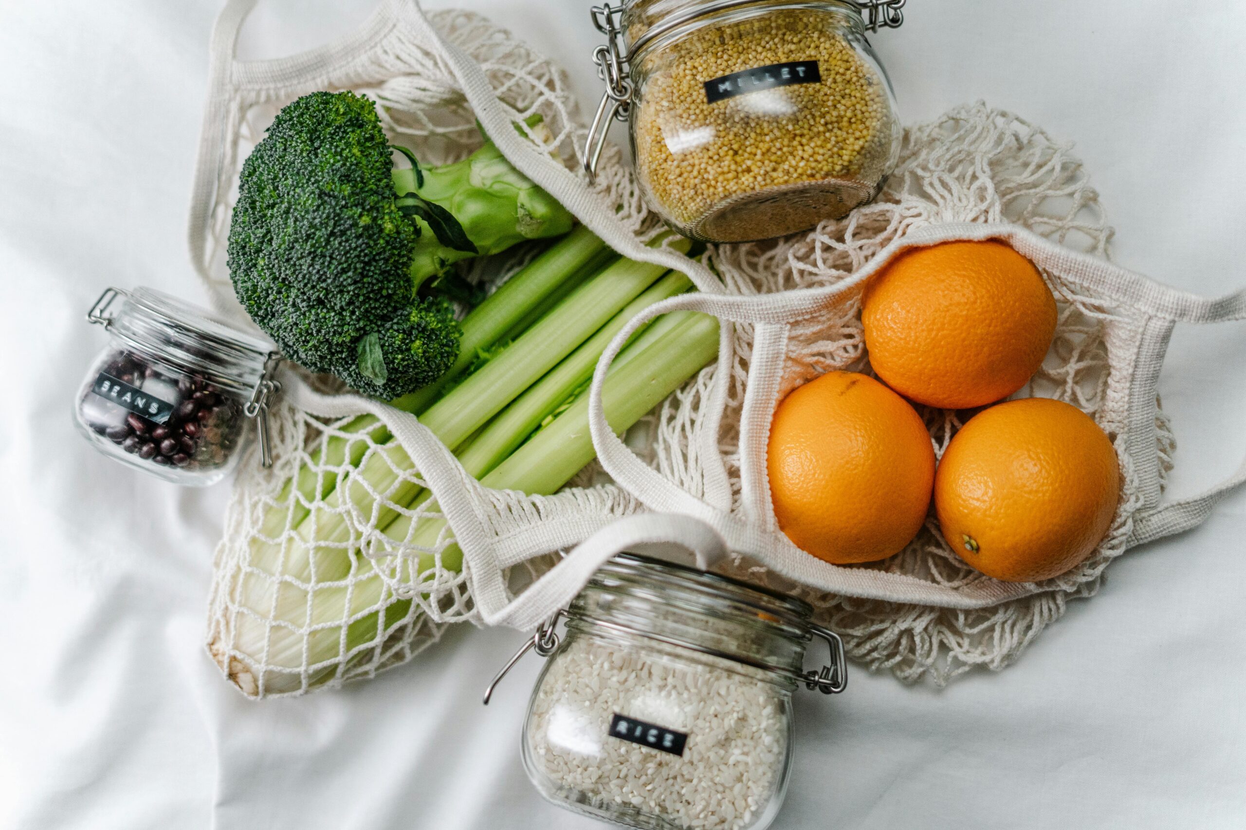 Ingredients for sustainable recipes including millet, rice, beans in glass jars, and fresh vegetables in a reusable tote bag